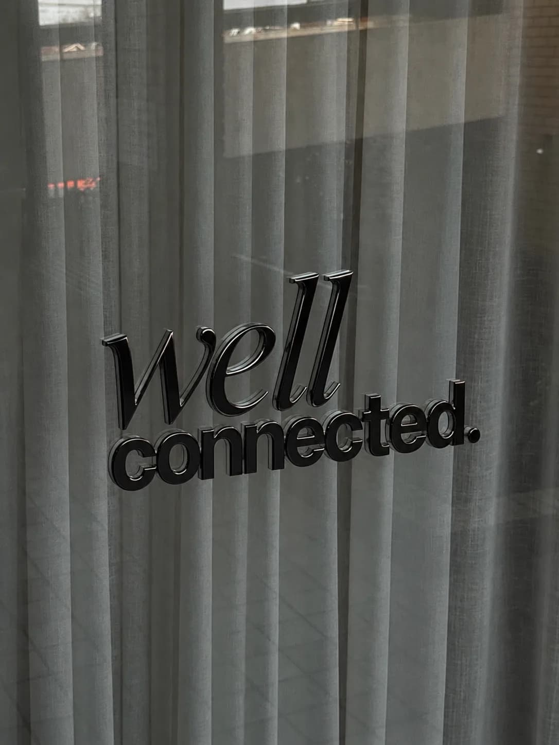 The well connected sign in polished black lettering against a sheer curtain